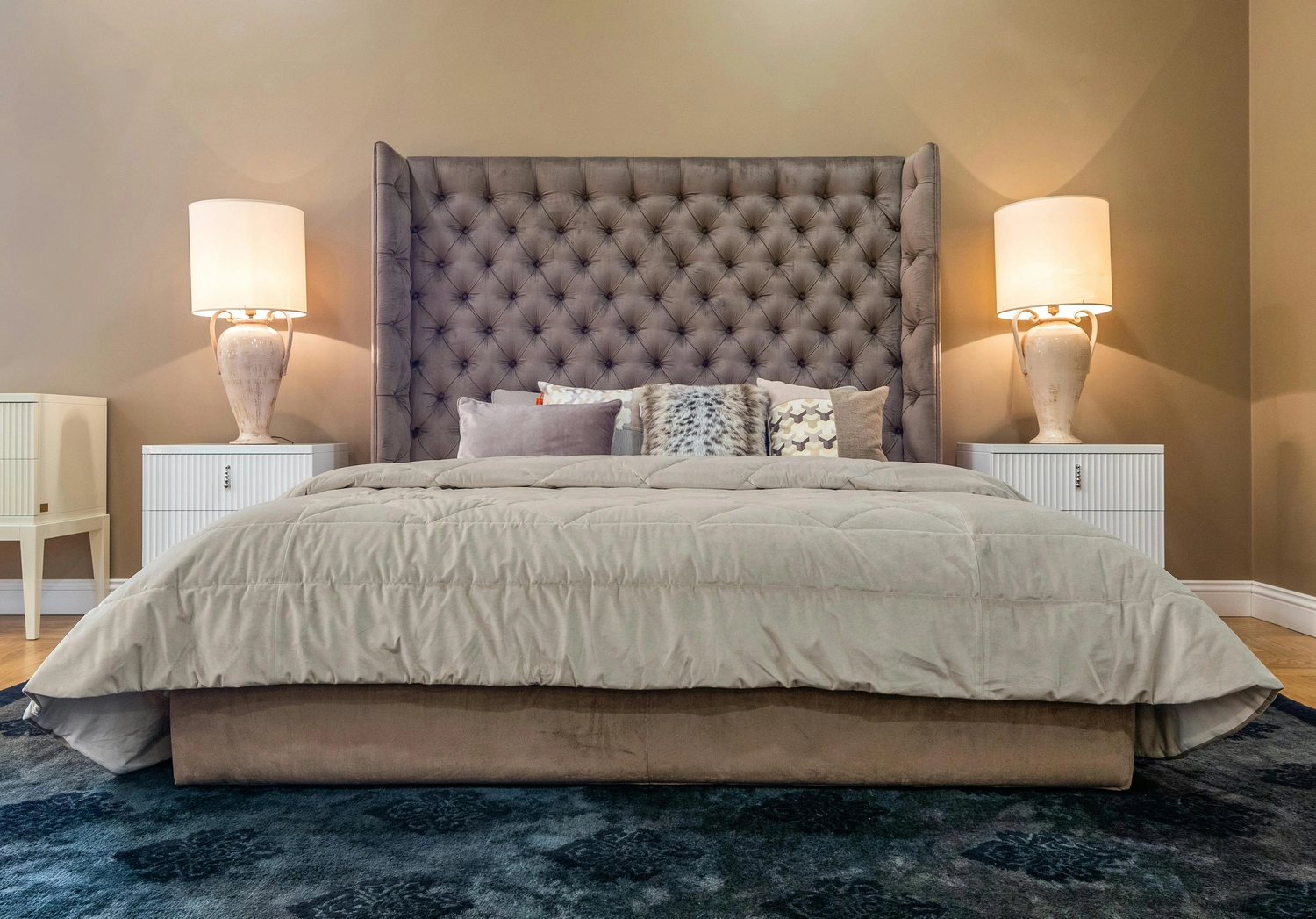 Polsterei Dorstel – fachmännische Handwerkskunst – Elegante Hauptschlafzimmereinrichtung mit einem luxuriösen grauen Polsterbett, getuftetem Kopfteil und modernem Dekor.